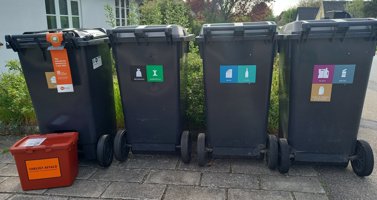 Viser affaldsbeholdere med klistermærker der skal sikre korrekt sortering.