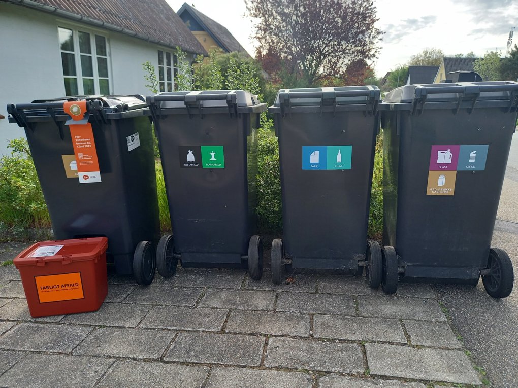 Viser affaldsbeholdere med klistermærker der skal sikre korrekt sortering.